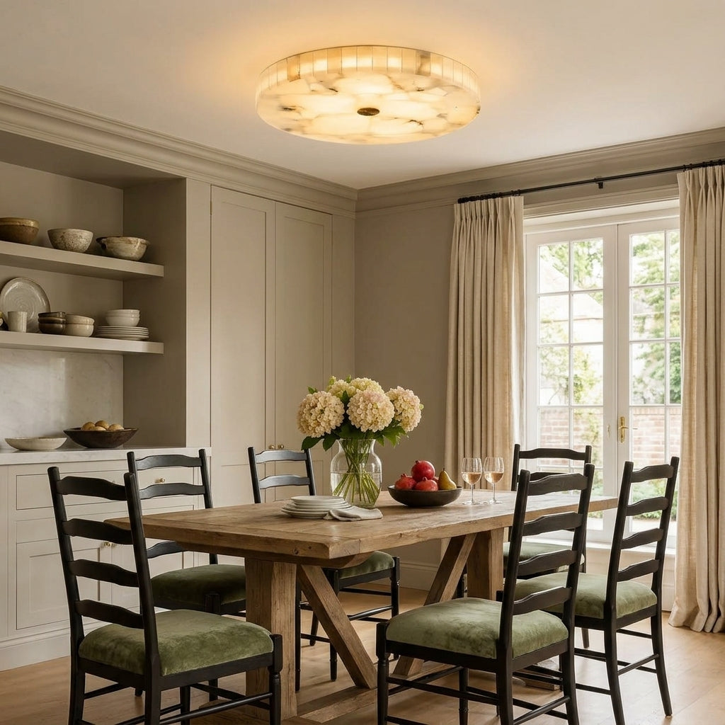 A round marble ceiling light fixture with a warm glowing glass or stone-like textured centre, mounted on a white ceiling in a styled dining room with a wooden table, chairs, and a window.