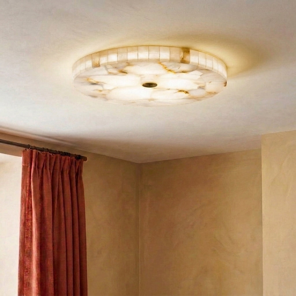 A round flush-mount marble ceiling light fixture, shown illuminated on a white ceiling in a room with beige walls and a red curtain.