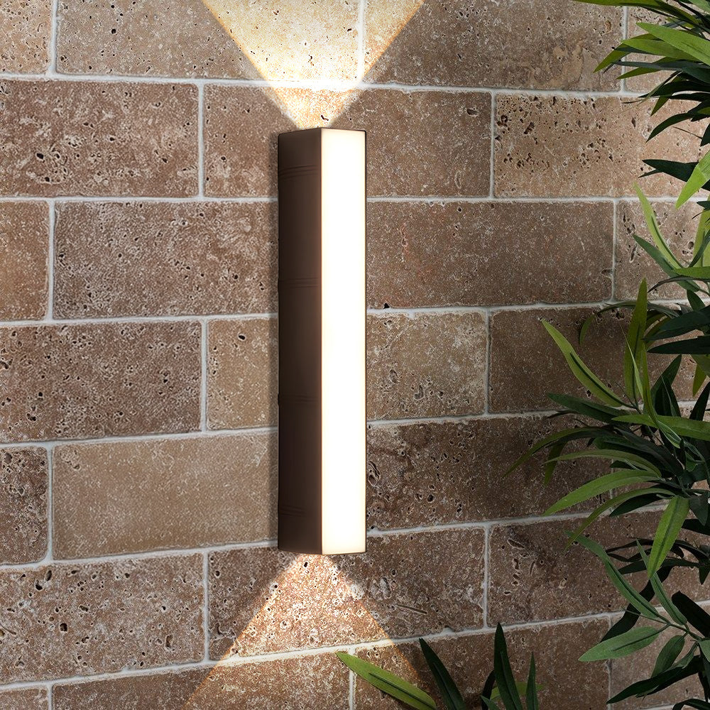 Black linear peqi outdoor wall light installed on a textured brick facade casting a warm V-shaped glow
