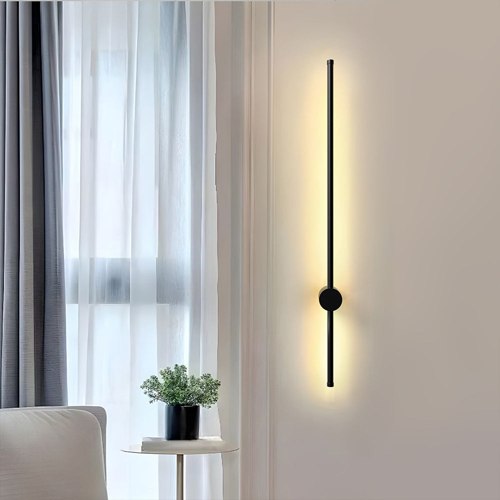 Long black pila LED tube wall light mounted vertically next to sheer curtains in a bright, modern room