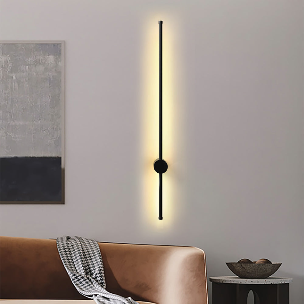 Warm ambient light radiating from a vertical rotatable linear pila wall fixture above a brown sofa