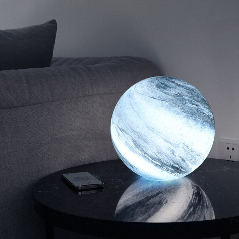 Blue pilo planetary globe lamp casting a soft ambient light on a dark glass living room table