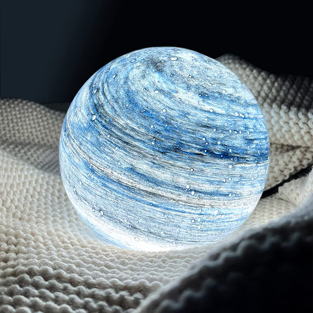 Cosy pilo blue glass orb lamp providing a soothing wash of light on a textured white knitted blanket