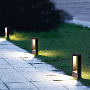qura modern black LED pathway bollard lights illuminating a paved residential walkway at dusk