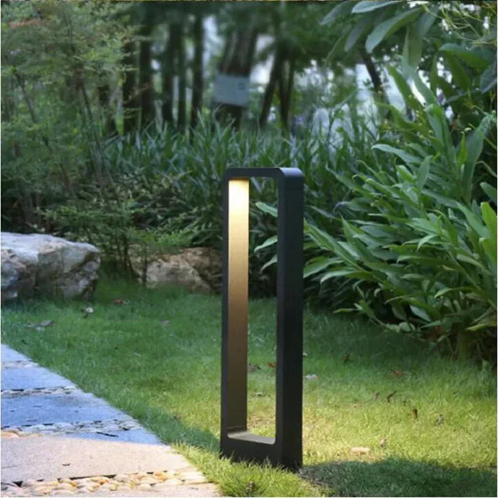 qura tall black rectangular LED garden bollard light installed on a lush green lawn