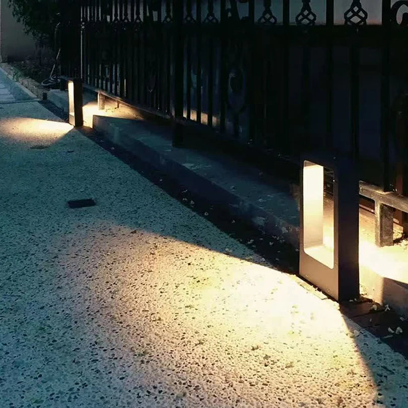 qura IP65 waterproof LED walkway bollard casting a warm downward glow along a path next to a fence