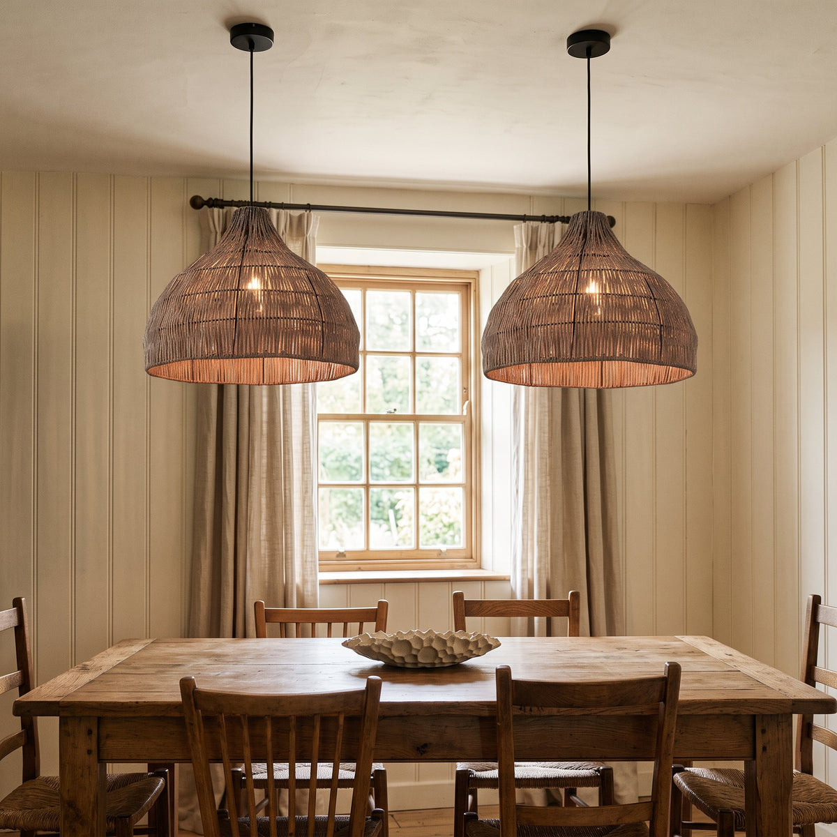 2 Relton rattan pendant lights hanging in front of a sash window in a cream British dining room
