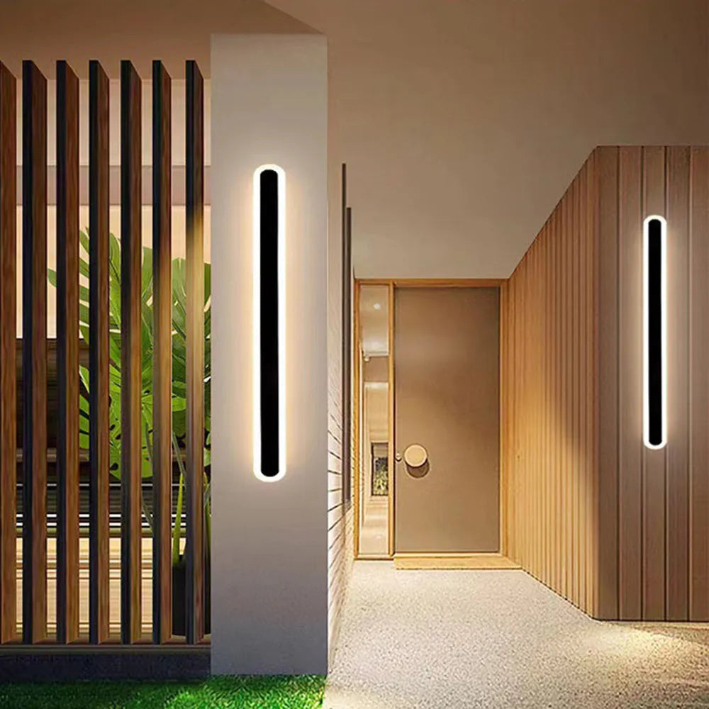 Riqi linear oval outdoor wall light installed on a garden wall and in a timber-clad hallway entrance at night
