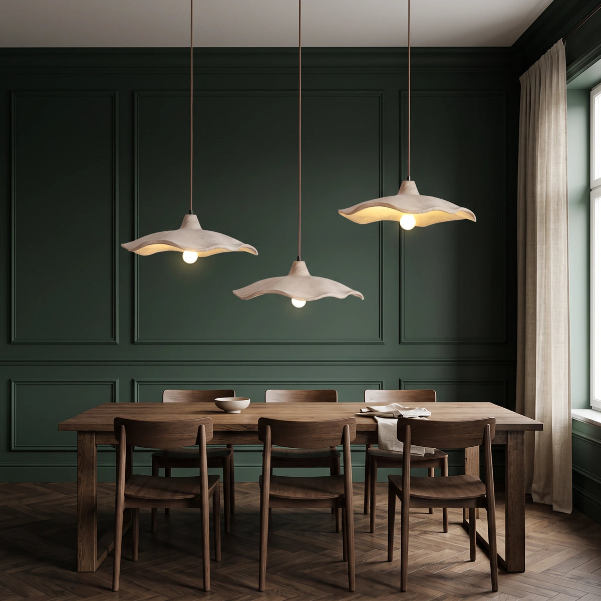 3 Rylin scalloped concrete bell pendant lights hanging above a long dark oak dining table in a deep green dining room