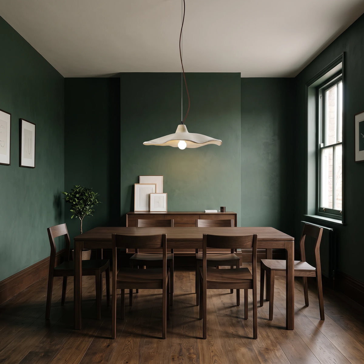 Rylin scalloped concrete bell pendant light hanging above a dark oak dining table in a deep green dining room