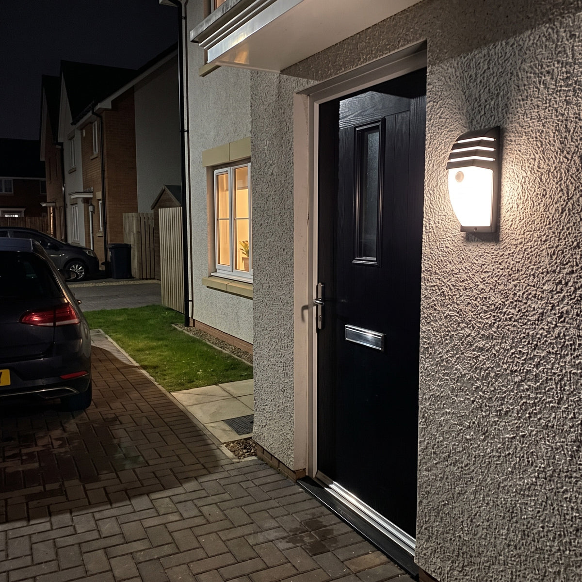 Large Strata outdoor wall light beside a black front door on a modern grey rendered house at night