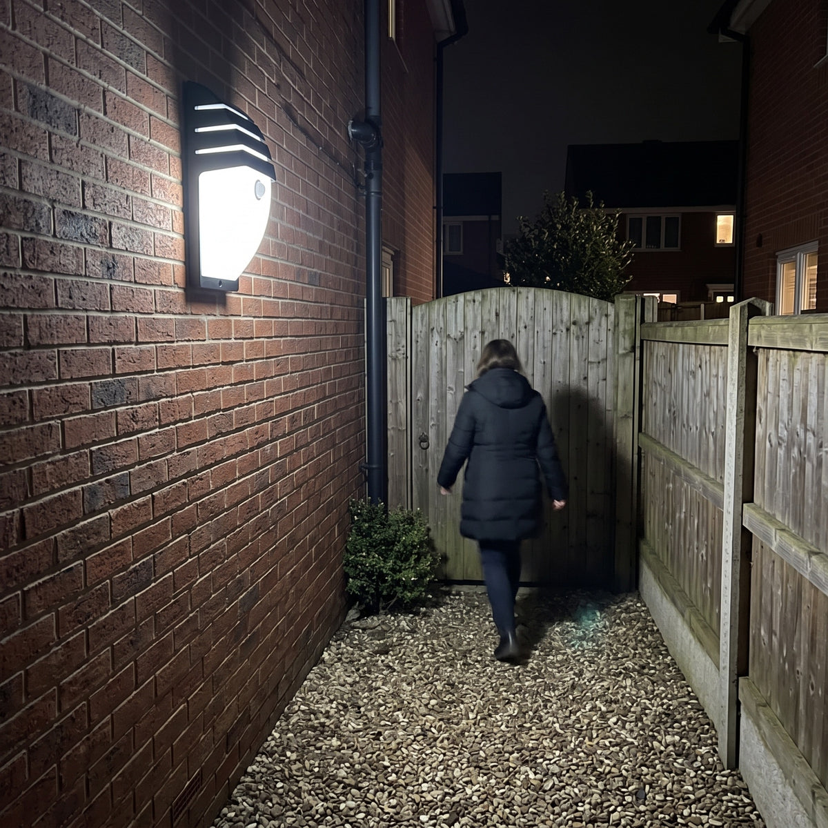 Strata motion sensor wall light switching on as a person walks along a side passage at night