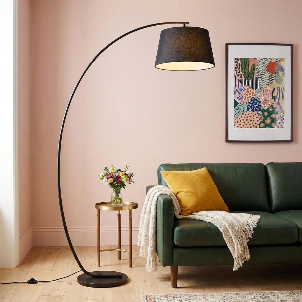 Tavio arc floor lamp with a black fabric drum shade beside a green leather sofa in a blush pink living room