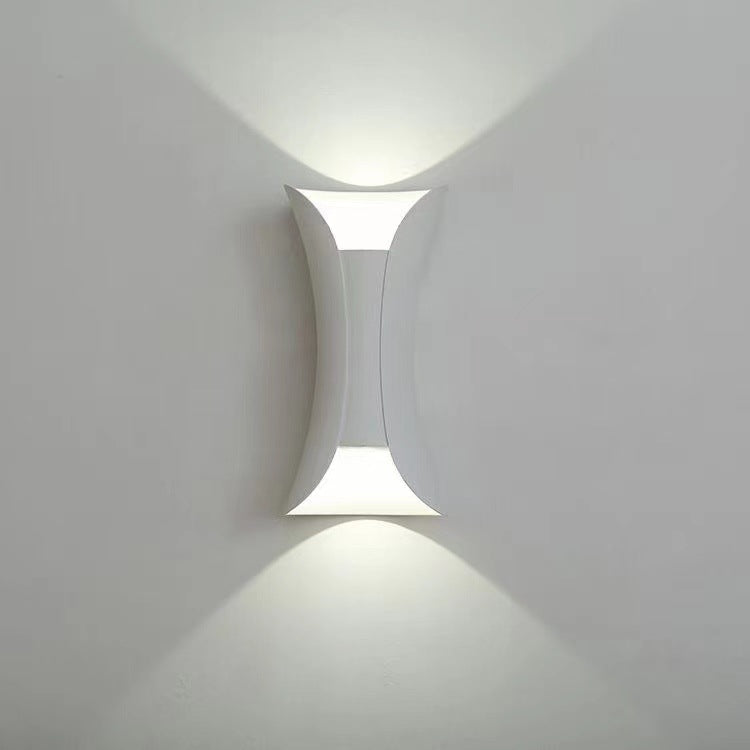 Sleek white teka modern hourglass LED wall sconce glowing crisply on a light wall