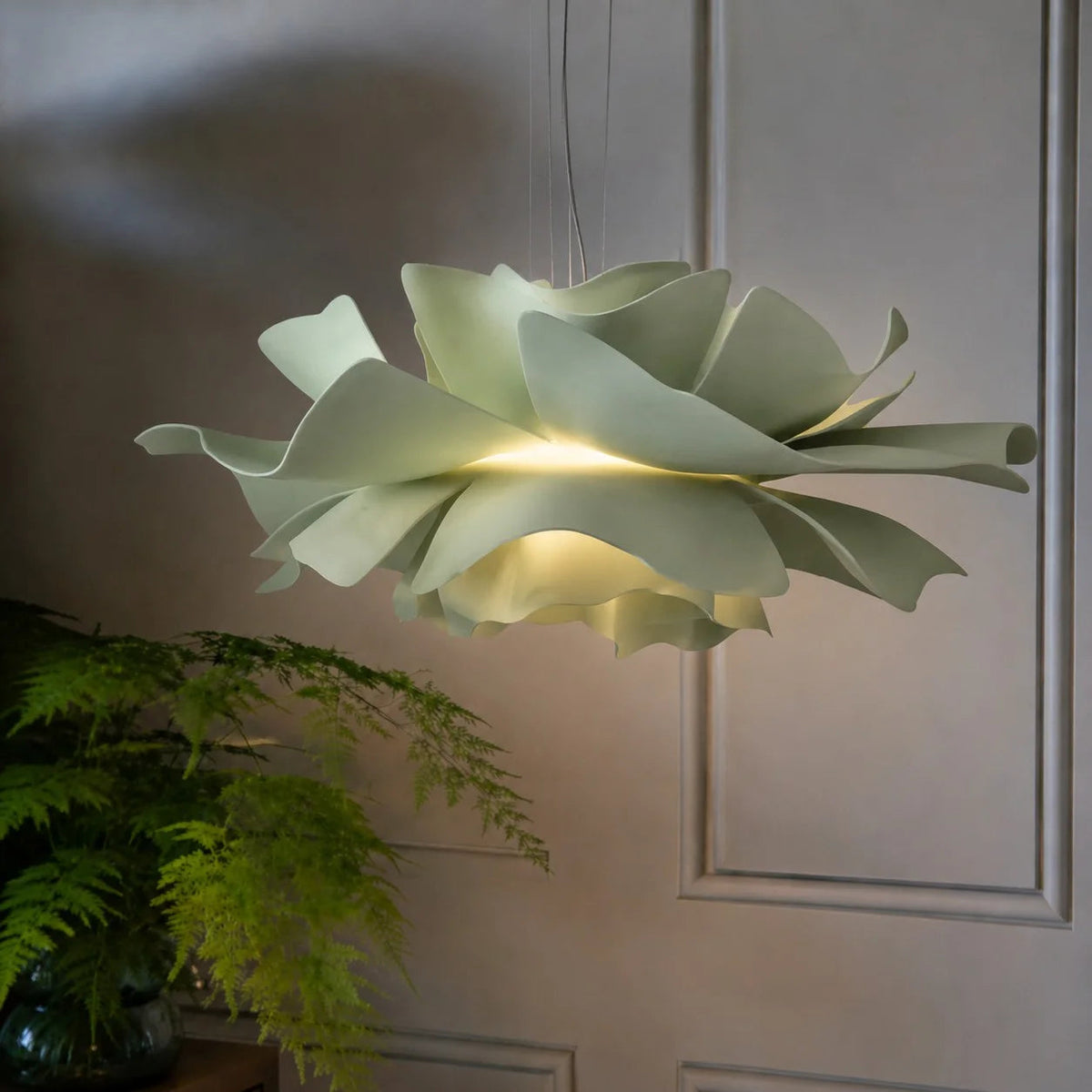 Close-up of the sage green telba acrylic floral pendant casting a warm glow in a botanical setting