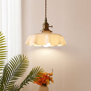 Vintage tugyl scalloped cream glass pendant light with antique brass hardware illuminating a bright corner with tropical plants