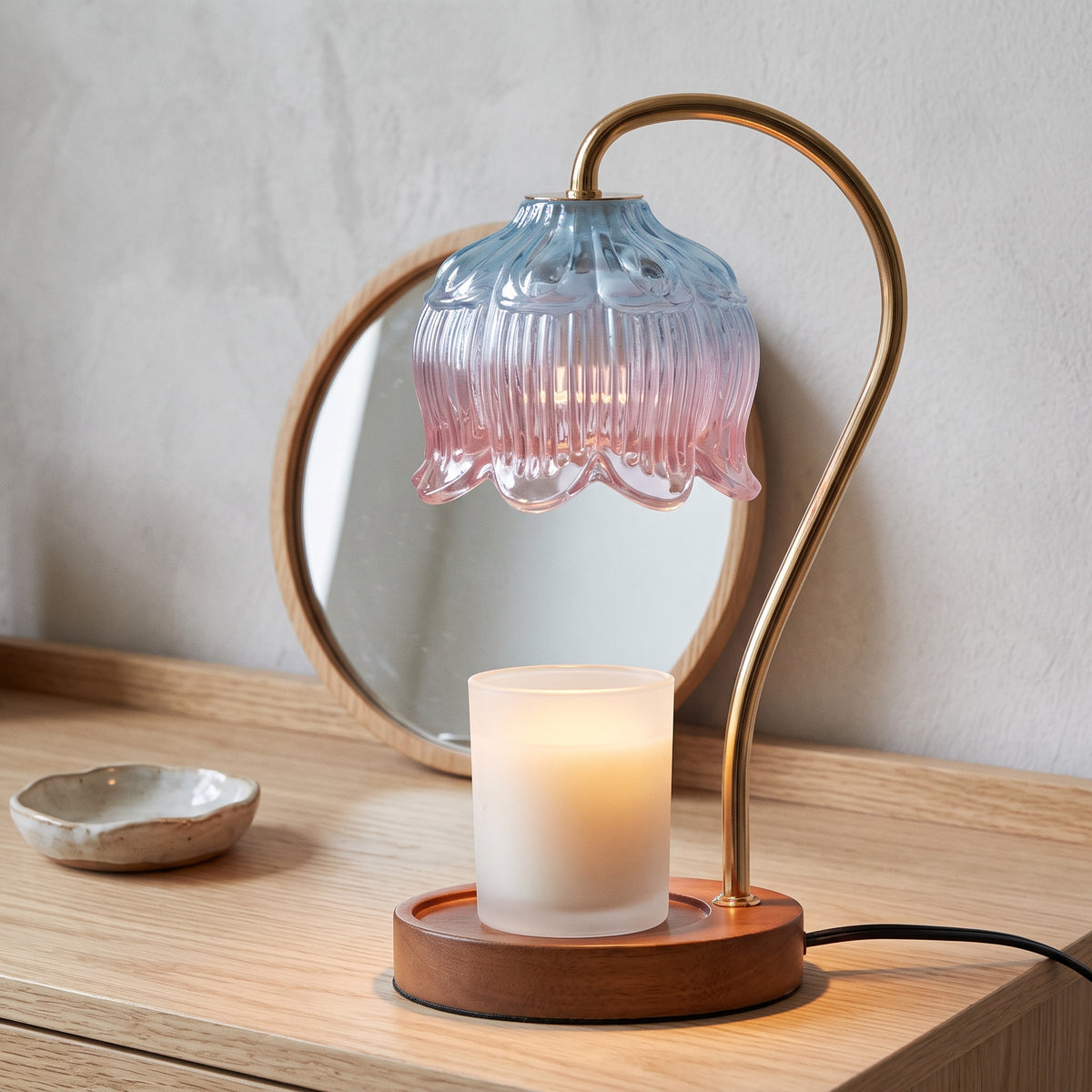 Tulvi blue to pink glass tulip candle warmer lamp on a wooden dressing table beside a round mirror