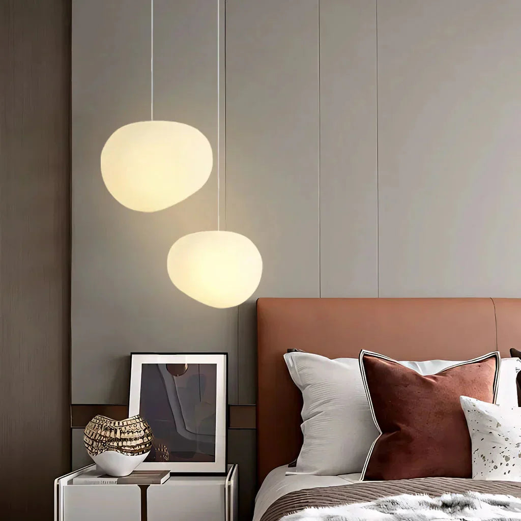 Pair of glowing glass tupel pendant lights acting as warm bedside lighting in a modern bedroom