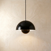 Modern tuska black mid-century flowerpot pendant light casting a warm downward glow against a textured wall