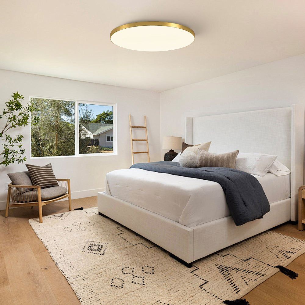 Minimalist gold round LED flush mount tywa light installed above a bed in a neutral interior