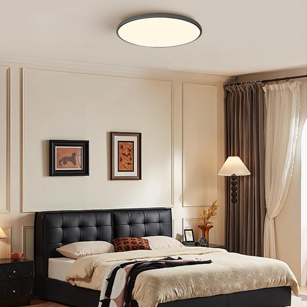 Silver round LED tywa ceiling light installed above a bed with a black headboard in a modern room
