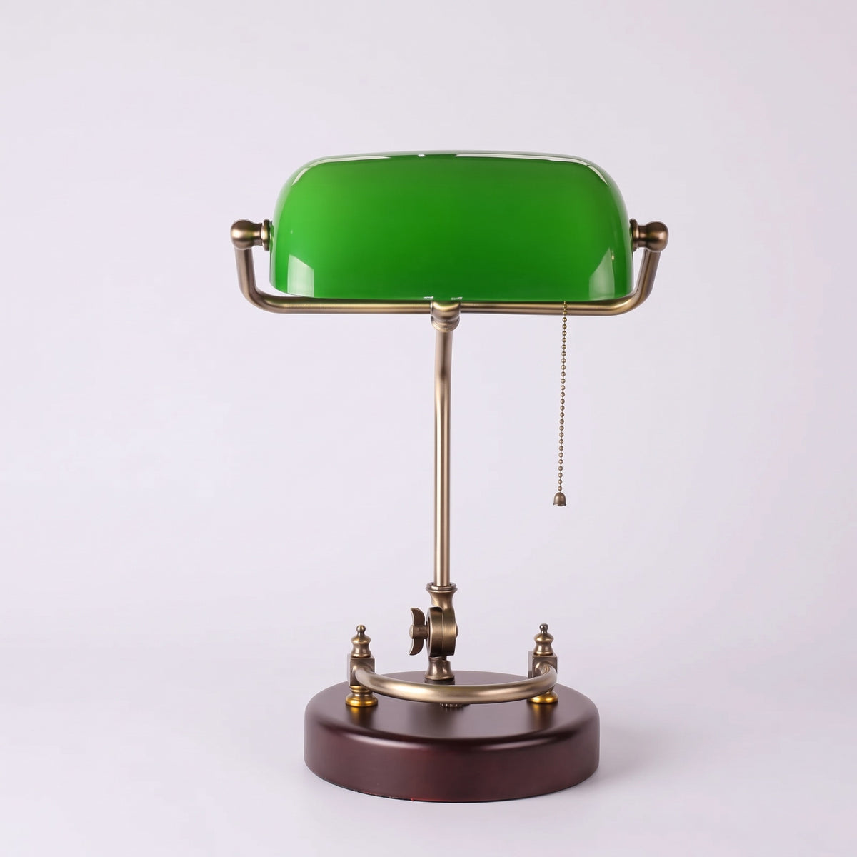 Verda green glass bankers lamp with a brass-finish arm and round wooden base on a light grey studio background