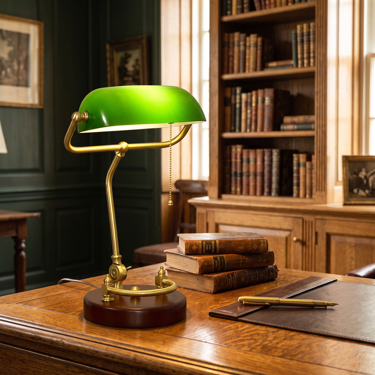 Verda green glass bankers lamp on a study desk beside a stack of leather-bound books and a brass fountain pen