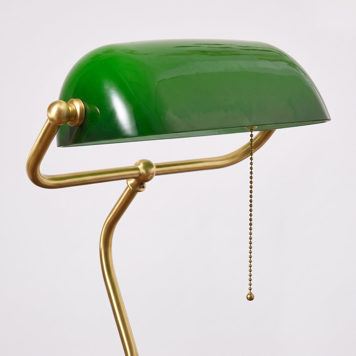 Close-up of the Verda green glass shade, brass-finish arm pivot for the 90° adjustment and pull chain on a light grey studio background