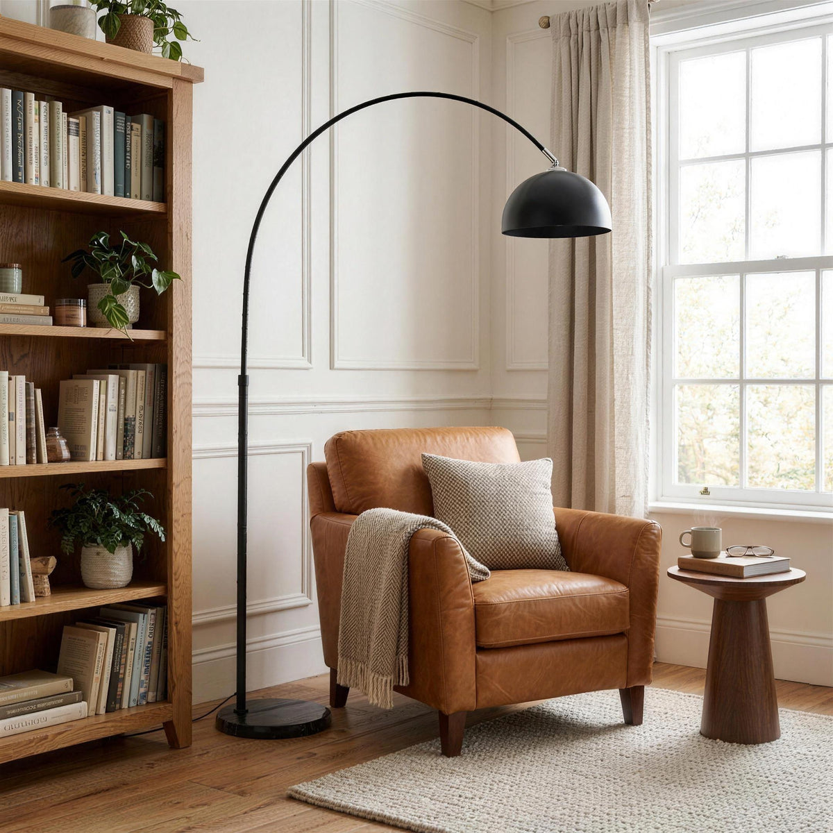 Black arc floor lamp over a caramel leather armchair in a reading corner