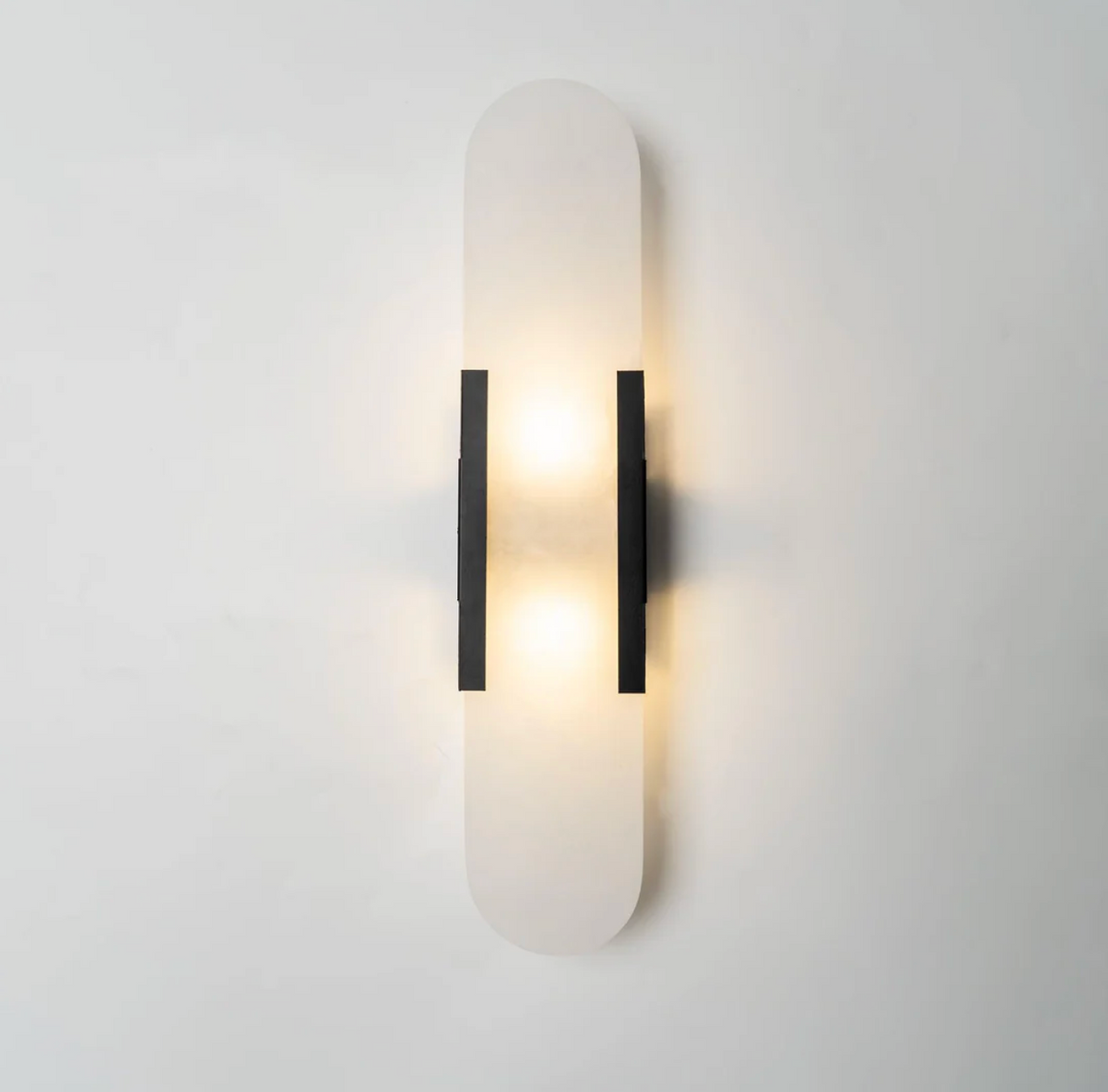 yuhy front view of the modern black hardware and natural marble pill sconce glowing softly